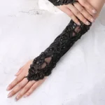 Black steampunk fingerless gloves with embroidered floral sequin details, sheer mesh inserts, and satin fabric - front top-down view on white wedding dress background