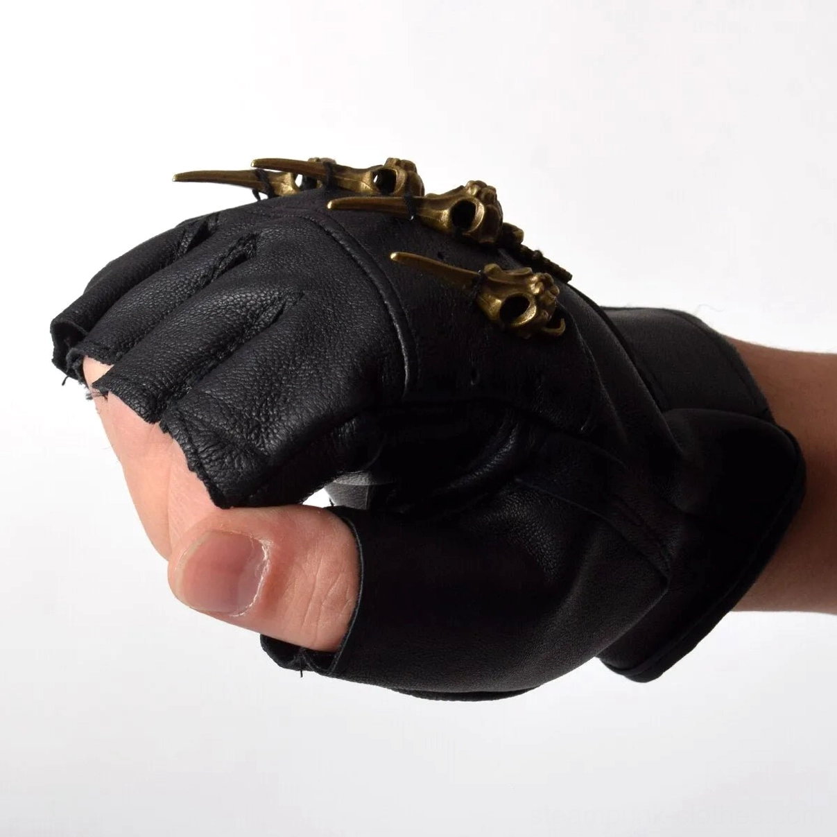 Side close-up of black fingerless steampunk leather gloves worn on male hand, partial brass skull decoration visible, industrial style