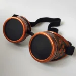 Steampunk goggles with reddish bronze metal finish and black elastic strap, flat lay top-down view on white background
