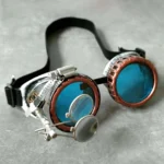 Handmade steampunk goggles with copper rim and blue polycarbonate lenses featuring magnifying loupes attachment, three-quarter overhead view