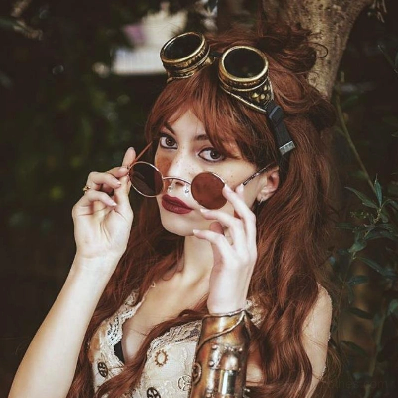 Red-haired model wearing bronze steampunk costume goggles outdoors with woodland background