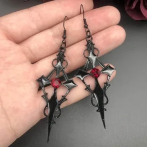 Gothic cross drop earrings held in palm showing matte black metal with red crystal center detail