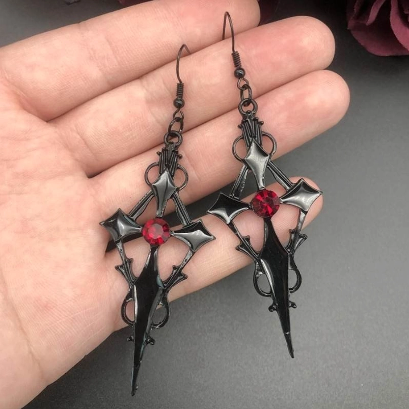 Gothic cross drop earrings held in palm showing matte black metal with red crystal center detail