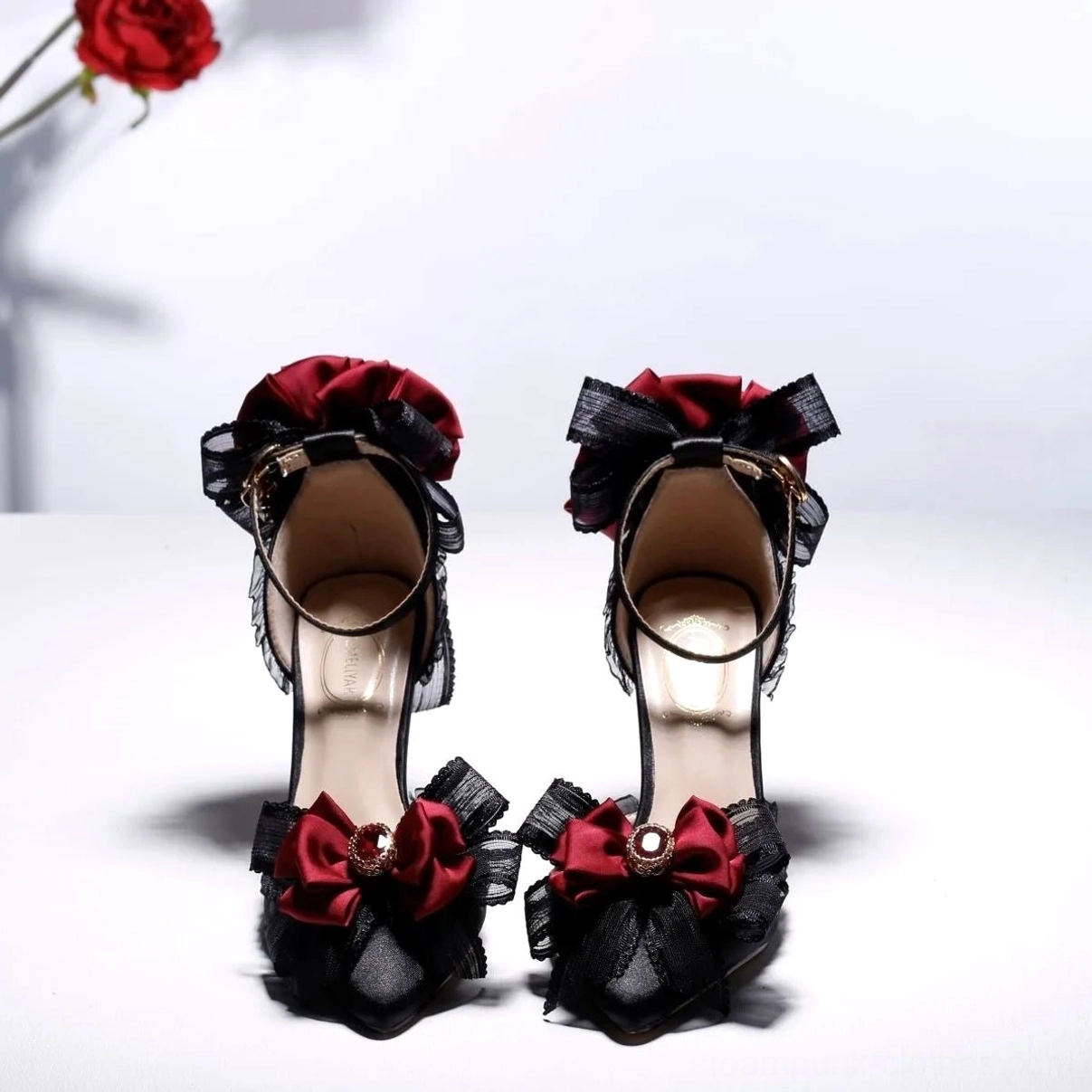 Black steampunk gothic high heel shoe front view featuring pointed upper, wine-red flower ornaments, delicate lace trim, and stiletto heel - straight frontal angle
