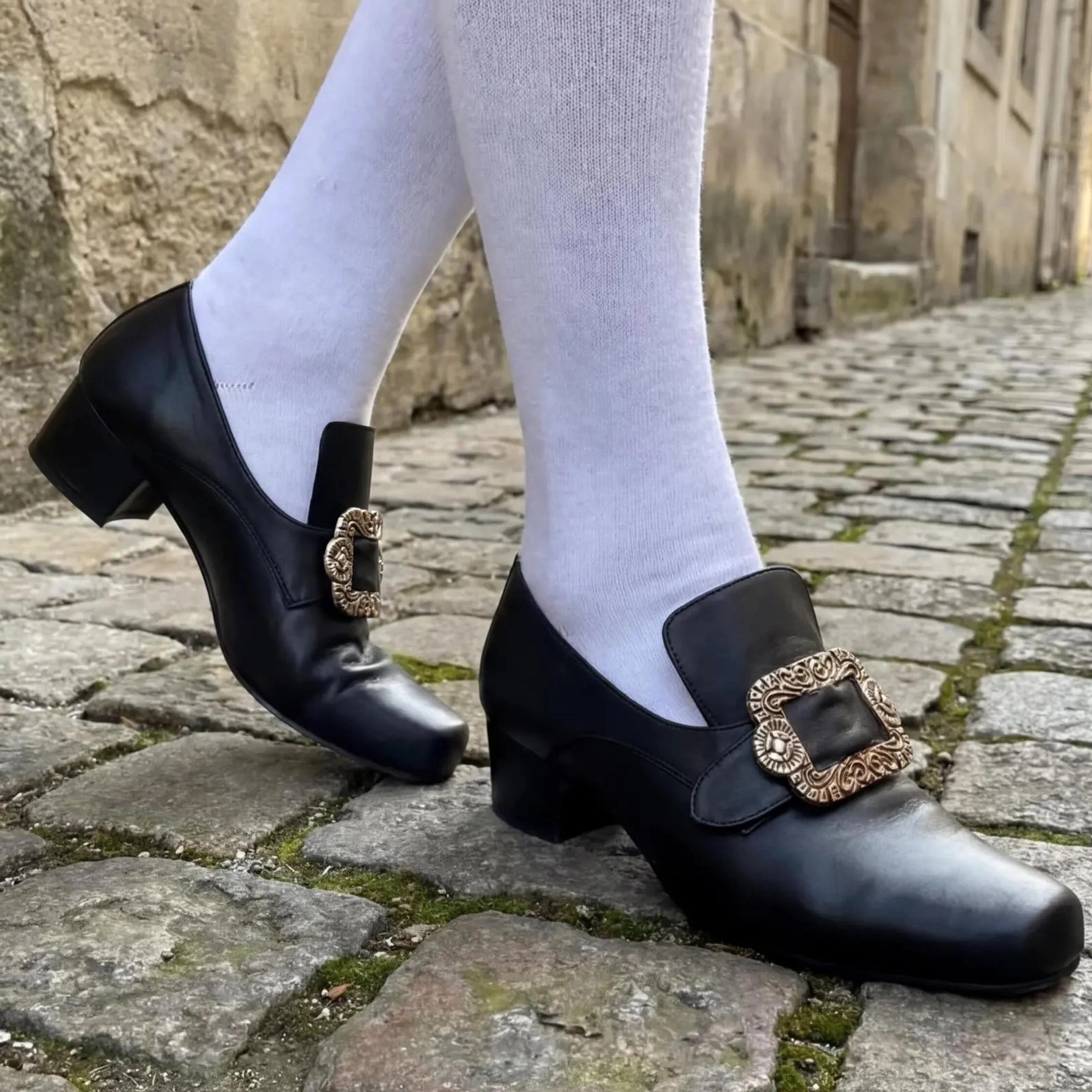 Steampunk gothic leather shoes with carved metal buckles, black leather, white knee-high socks, low angle side view cobblestone street