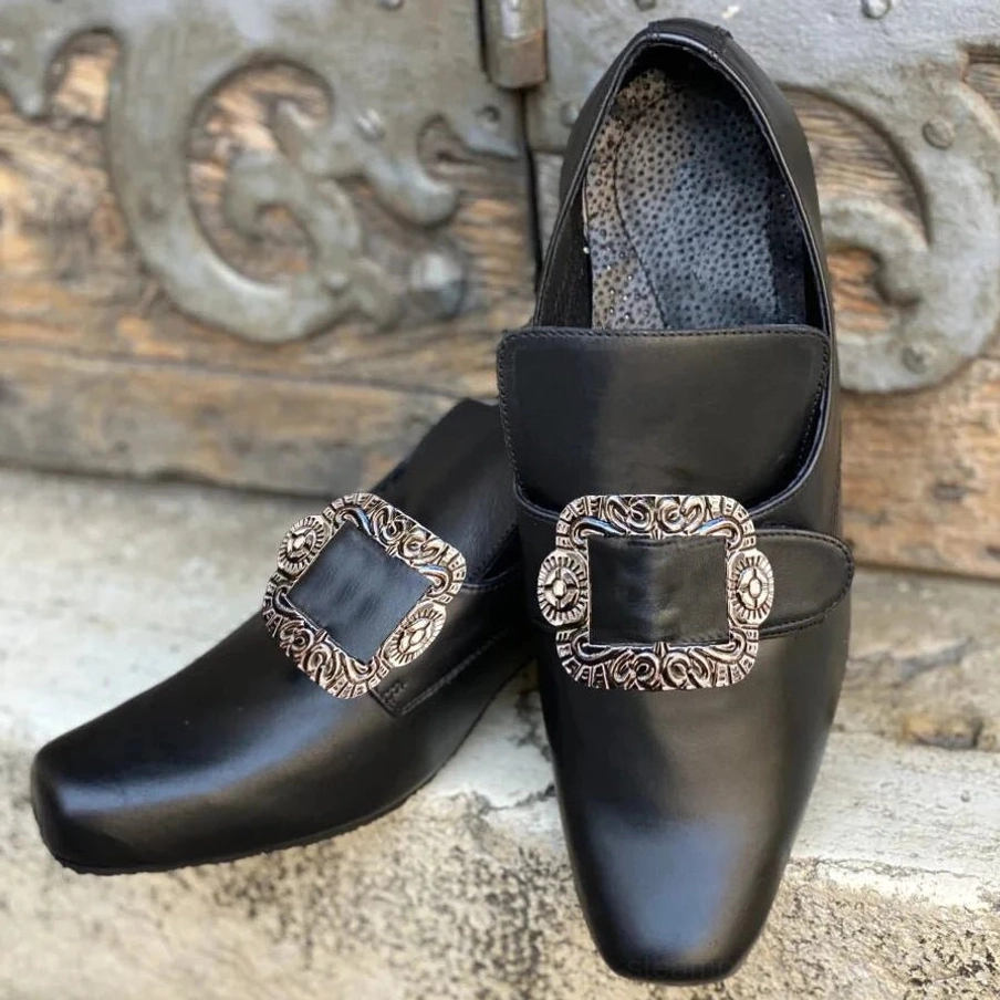Steampunk gothic medieval leather shoes front flat view, polished black leather, ornate square buckles, perforated insole detail, vintage metal door background