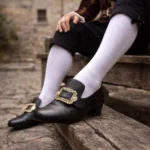 Steampunk gothic medieval leather shoes with ornate carved metal buckle, black smooth leather, low block heel, side close-up view on wooden bench