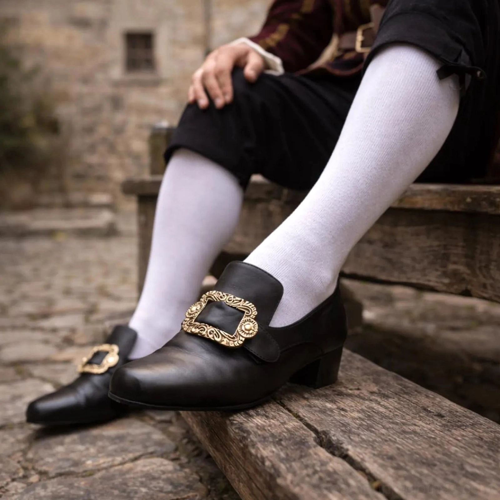 Steampunk gothic medieval leather shoes with ornate carved metal buckle, black smooth leather, low block heel, side close-up view on wooden bench