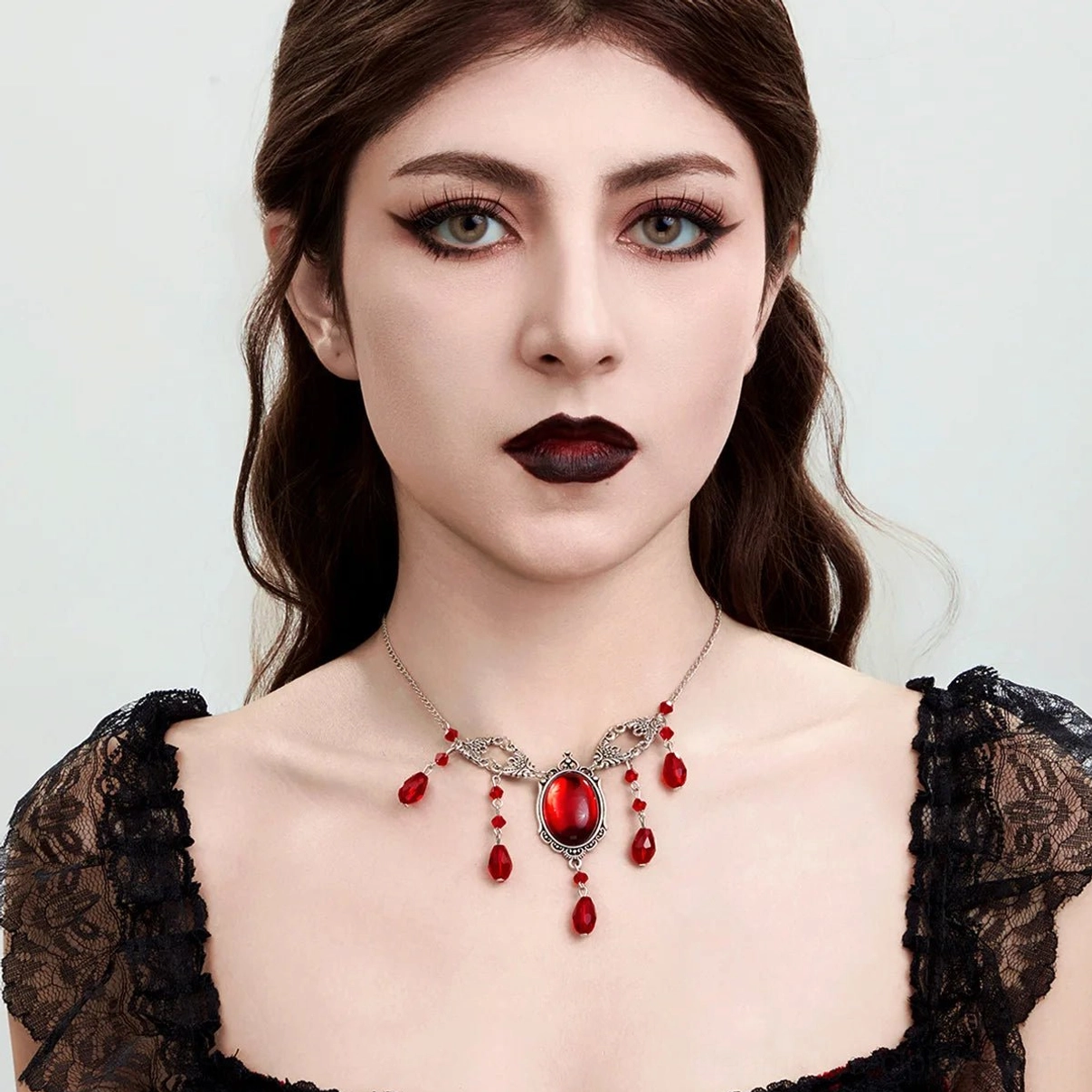 Frontal portrait of gothic steampunk vampire choker necklace worn by model in black lace puff-sleeve dress, displaying intricate filigree design and crimson gemstone accents in minimalist studio setting