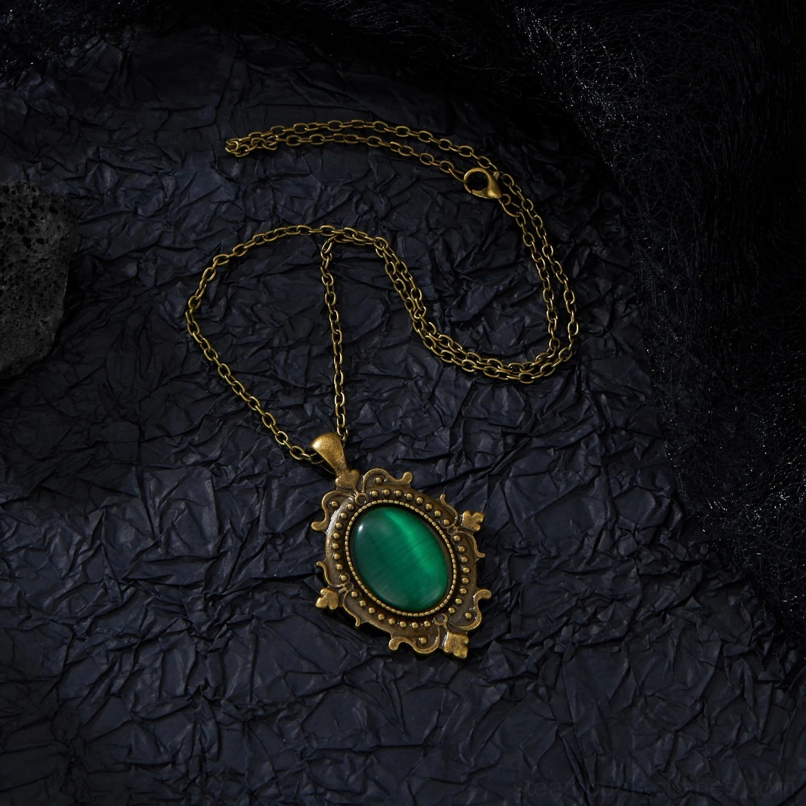 Antique bronze cable chain with ornate oval green cabochon pendant flat lay on black fabric background