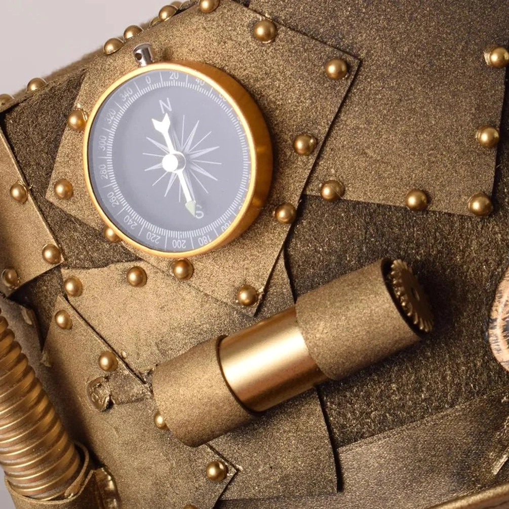 Close-up macro shot of steampunk hat details: compass, brass telescope, and riveted metal texture