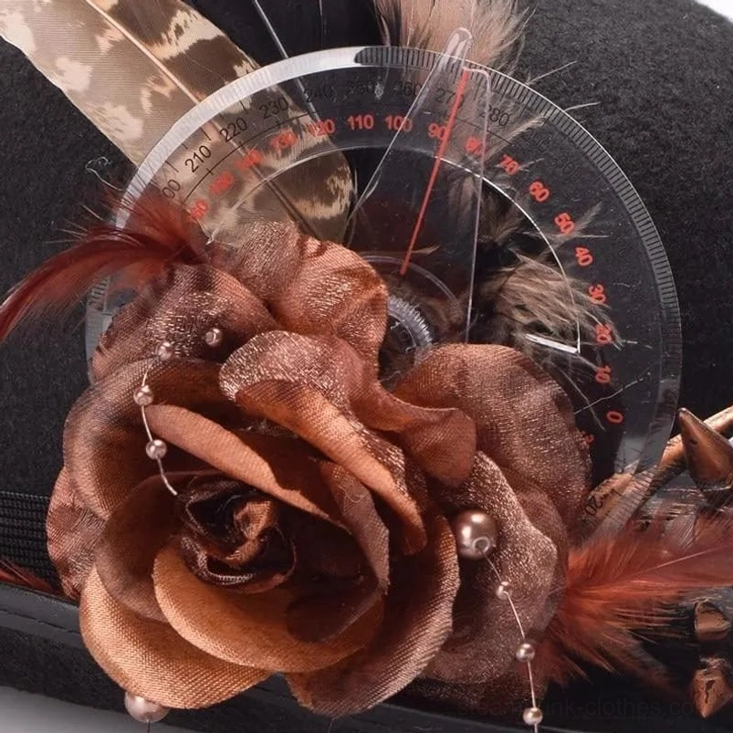 Close-up macro detail of steampunk hat decorations featuring brown fabric rose, feathers, brass gears, protractor elements and bead pendants