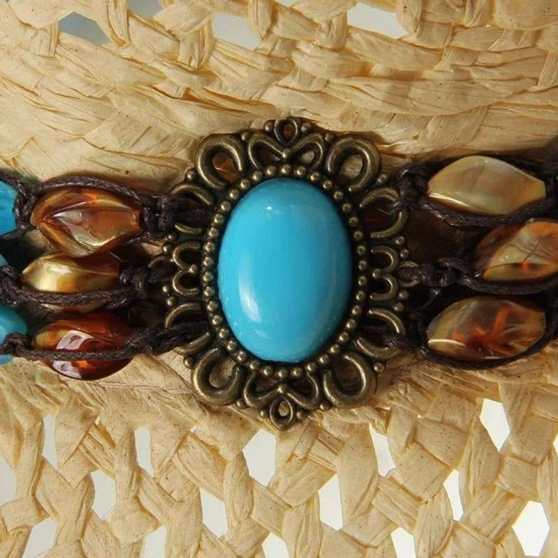 Macro photography of central steampunk hat ornament featuring ornate bronze frame, large turquoise cabochon stone and surrounding decorative bead arrangement
