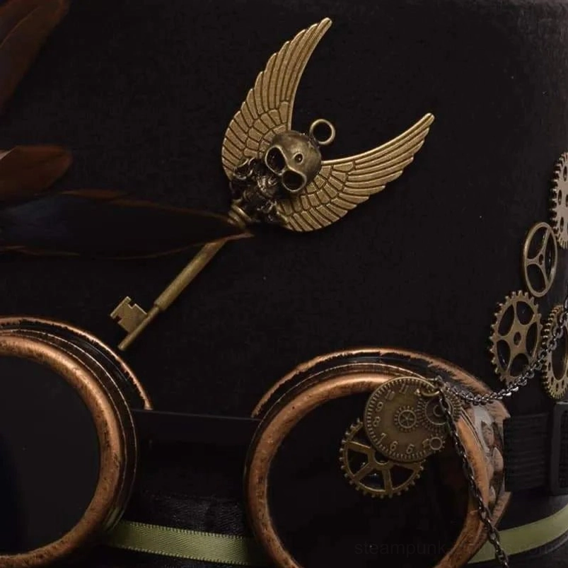 Steampunk top hat front close-up featuring winged skull key, bronze goggles, small gear charms, and green ribbon trim accent
