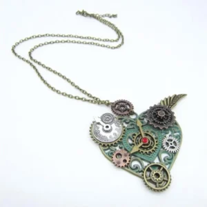 Steampunk heart necklace with mixed metal gears, patina green frame, red central gemstone, and wing ornaments displayed in oblique side view on white background