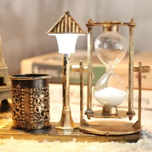 Steampunk hourglass pen holder lamp with gold bronze tone, unlit, positioned with book backdrop and white sand timer visible