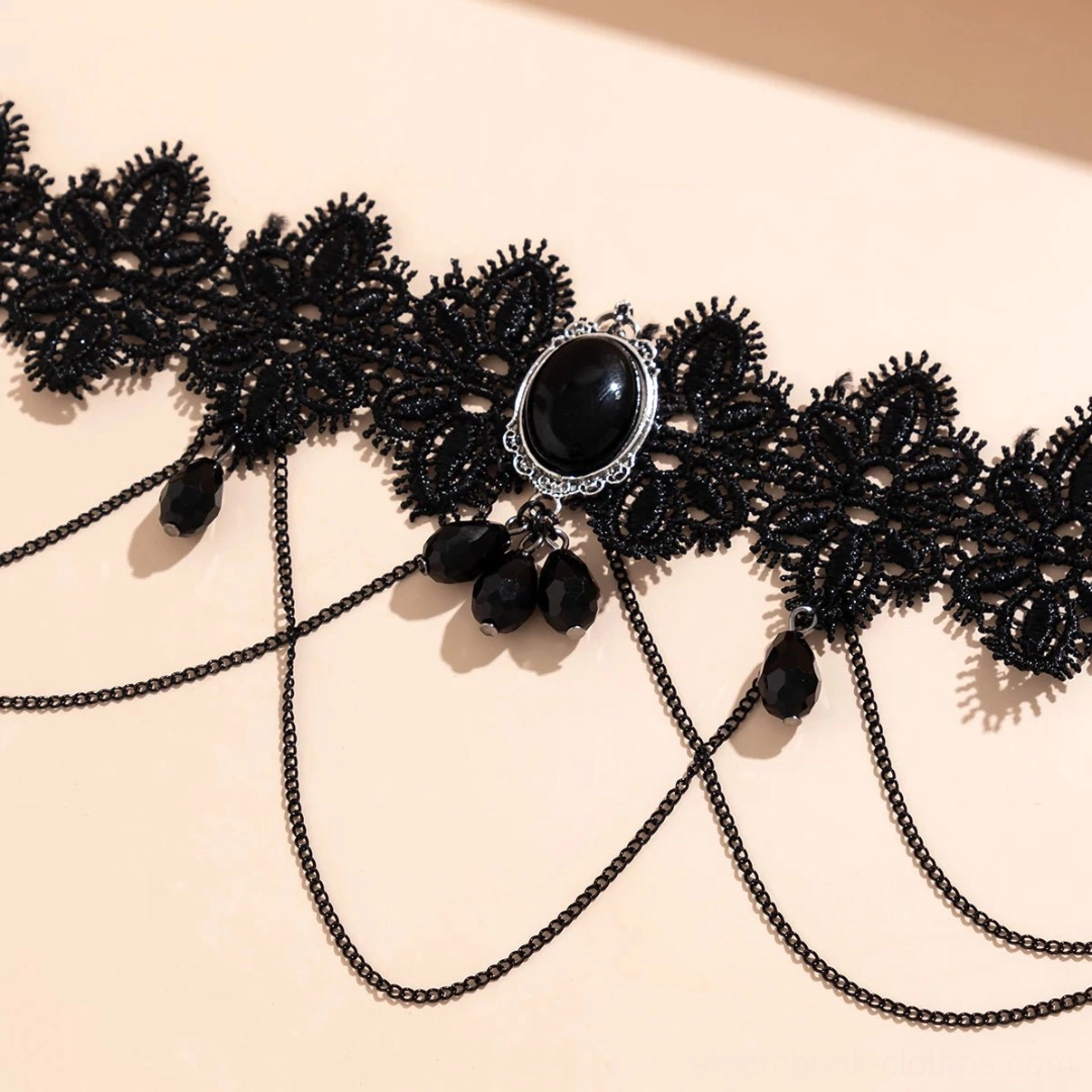 Extreme close-up of lace choker showing delicate black floral pattern, silver-framed black gemstone, crossed metal chains, and black teardrop bead embellishments with precision craftsmanship detail