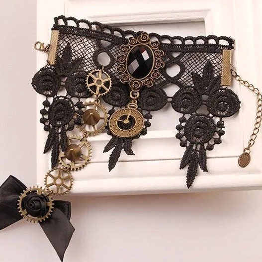 3/4 angled flat shot of steampunk lace hand jewelry with black lace, bronze mechanical charms, bow accent, and dangling metal chain on wooden background