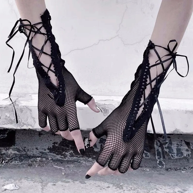 Black fingerless gloves with fishnet mesh, scalloped lace trim, and cross-ribbon lacing detail viewed from side angle, showcasing steampunk gothic hand wear on female model with cracked concrete background