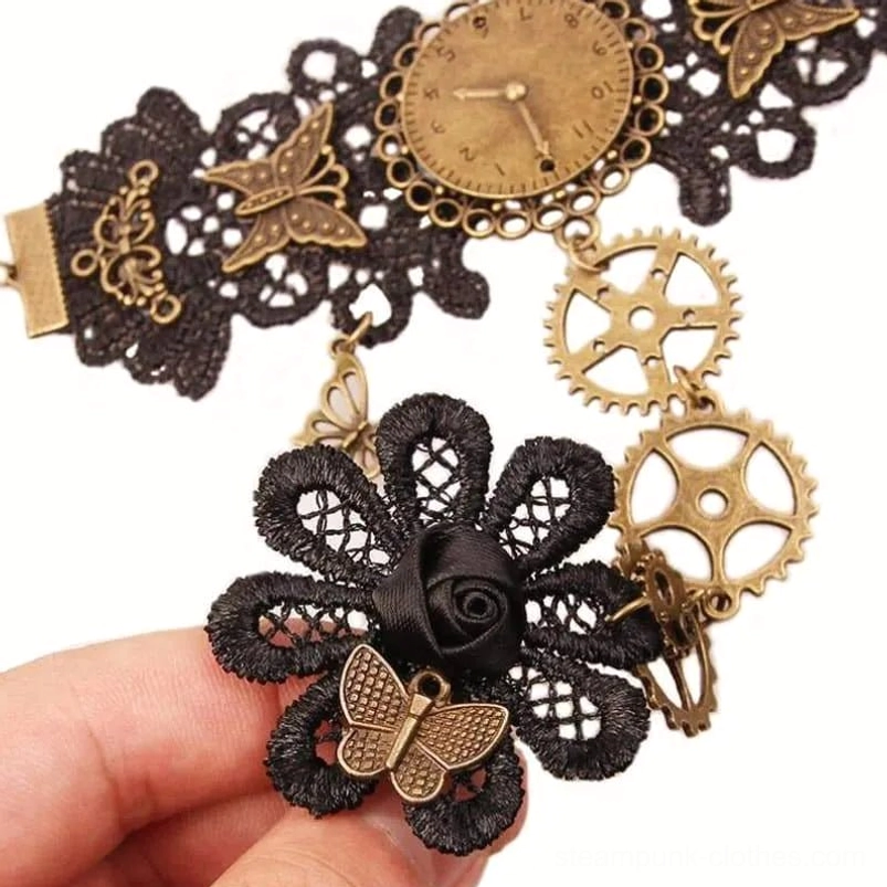 Steampunk lace gloves jewelry detail showing black floral lace with rose center, bronze butterfly and gear charms, top-down view on fingertips