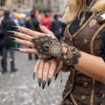 Steampunk lace hand glove with bronze gear decorations worn on female model with black nail polish, outdoor street fair setting showcasing Victorian-gothic style