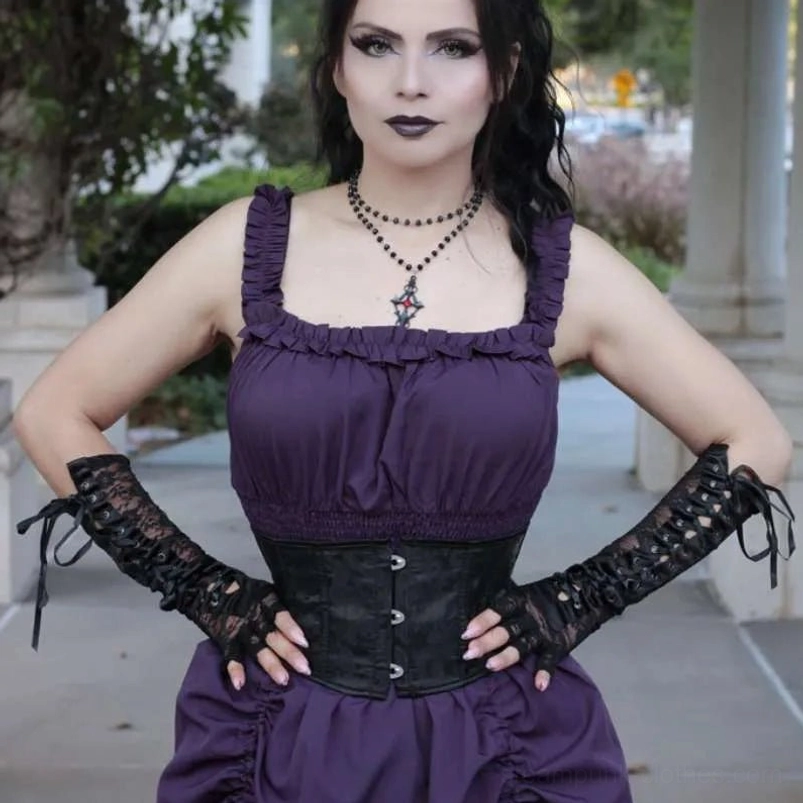 Goth model wearing black steampunk lace-up long gloves with metal eyelets paired with purple goth dress and corset outdoors
