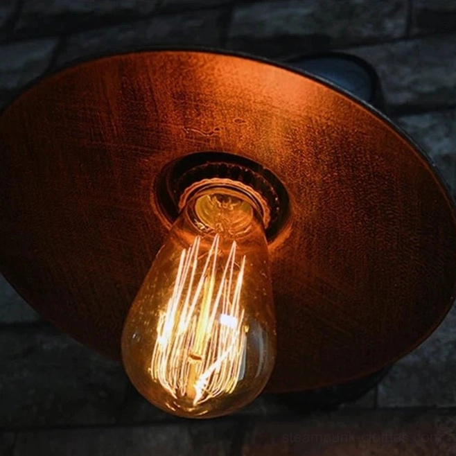 Steampunk wall sconce lamp shade and exposed filament Edison bulb glowing in dim indoor setting, close-up overhead view of distressed copper metal shade