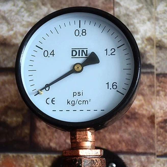 Pressure gauge component of steampunk lamp, white dial with black casing and DIN markings showing psi and kg/cm² measurements, close-up detail view