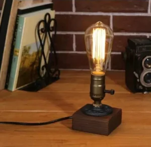 Steampunk table lamp with single vintage Edison bulb and rotary side switch, displayed on wooden table with brick wall backdrop and industrial decor
