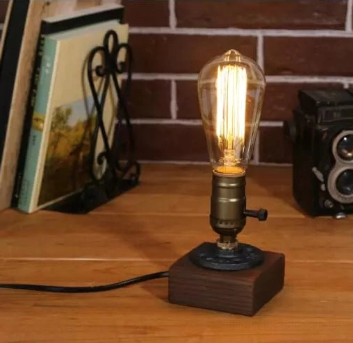 Steampunk table lamp with single vintage Edison bulb and rotary side switch, displayed on wooden table with brick wall backdrop and industrial decor