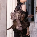 Steampunk vintage leather backpack with prominent winged armor emblem and brass rivets, worn by female model in off-shoulder top at historic architectural location, showcasing rear profile design