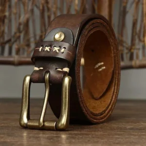 Full-grain dark brown leather steampunk belt with antique brass double pin buckle, cross-stitch detailing, and engraved strap patterns, displayed on wooden surface—front perspective view showing industrial craftsmanship and vintage aesthetic