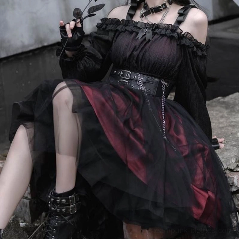 Seated low-angle view of gothic lolita steampunk dress showcasing off-shoulder strap detail, layered tulle skirt, styled with black combat boots and black rose prop on concrete rooftop