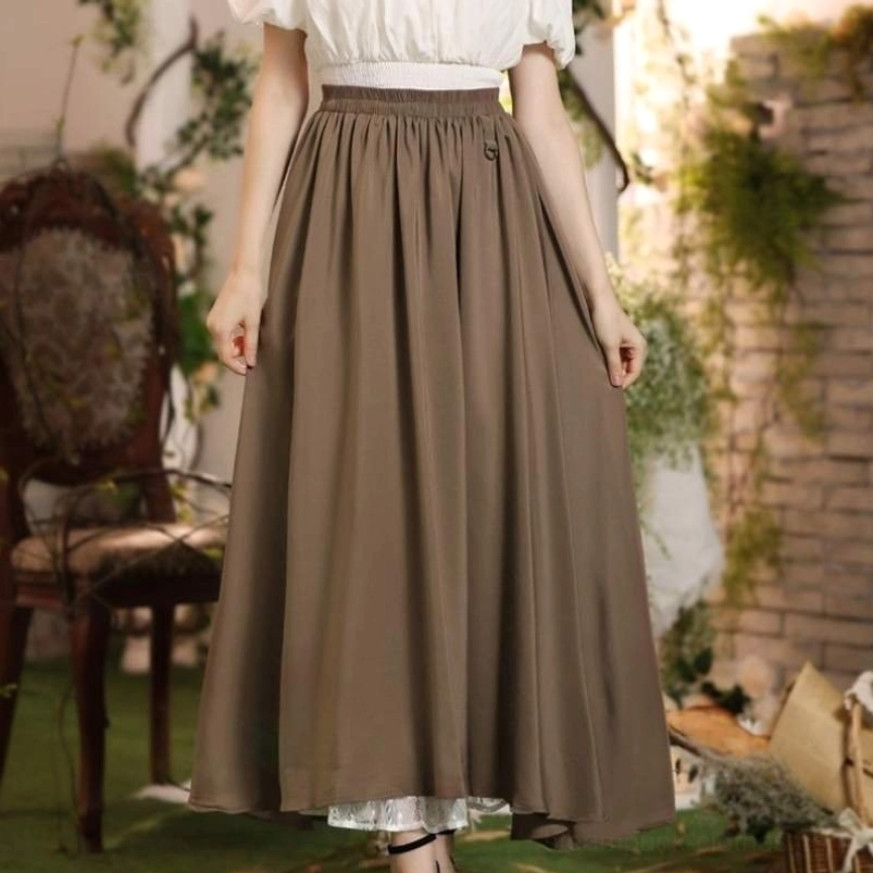 Flowy high-waisted brown maxi steampunk skirt with elastic waistband and lace-trimmed hem, worn by female model in garden courtyard, full-length front view