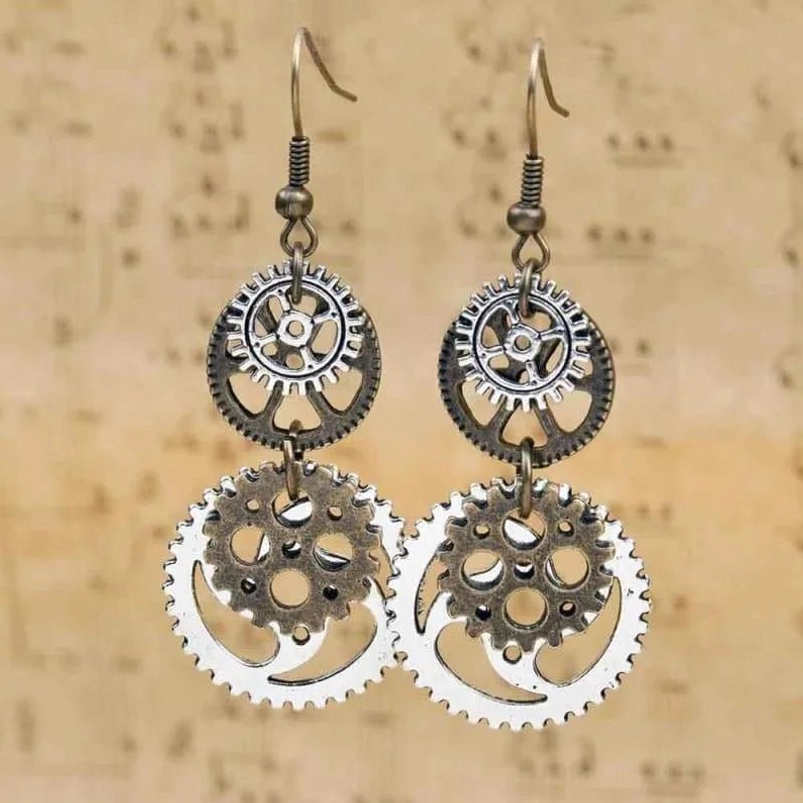 Symmetrical steampunk gear earrings featuring spring detail on ear hooks, flat lay display on beige vintage sheet music background showing mechanical craftsmanship