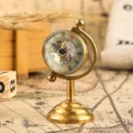 Steampunk mechanical globe desk clock with exposed brass gears and Roman numeral dial, antique brass finish, displayed on vintage map desktop setup