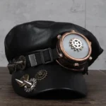 Steampunk military cap front three-quarter view showing black faux leather construction, integrated bronze aviator goggles, brass gear ornaments, and spike accents on structured crown