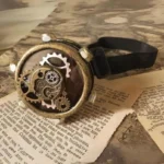 Steampunk monocle goggle with weathered bronze metal frame and exposed gear details, shown on vintage paper background with elastic strap visible