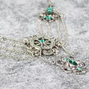 Close-up overhead view of multi-strand steampunk necklace featuring antique silver metal, green gemstones, and ornate gear-themed pendants