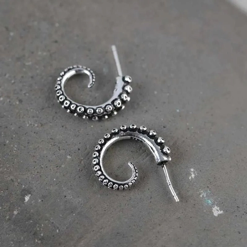 Top-down overhead view of antique silver octopus tentacle earrings showing detailed suction cup patterns and ear post findings on grey concrete surface