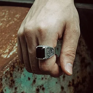 Steampunk onyx signet ring on male hand displaying ornate filigree details and polished silver finish against rustic weathered metal surface