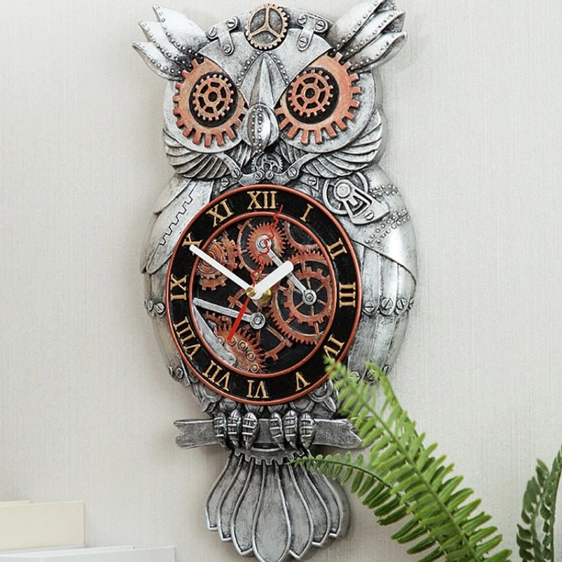 Distressed silver steampunk owl clock full body shot against light wall with green foliage backdrop, showcasing hand-carved resin construction and exposed gear design elements