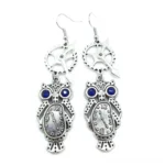 Steampunk owl dangle earrings with antique silver finish, blue rhinestone eyes, and clock dial mechanism - flat lay frontal view on white background