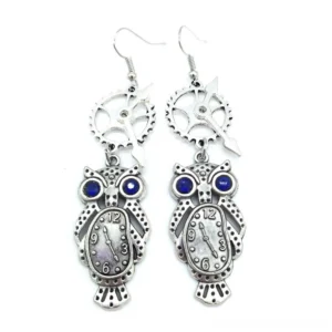 Steampunk owl dangle earrings with antique silver finish, blue rhinestone eyes, and clock dial mechanism - flat lay frontal view on white background