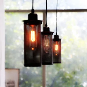 Multiple steampunk pendant lights with dark metal mesh shades suspended at varying heights, warm glowing Edison bulbs creating atmospheric industrial lighting installation