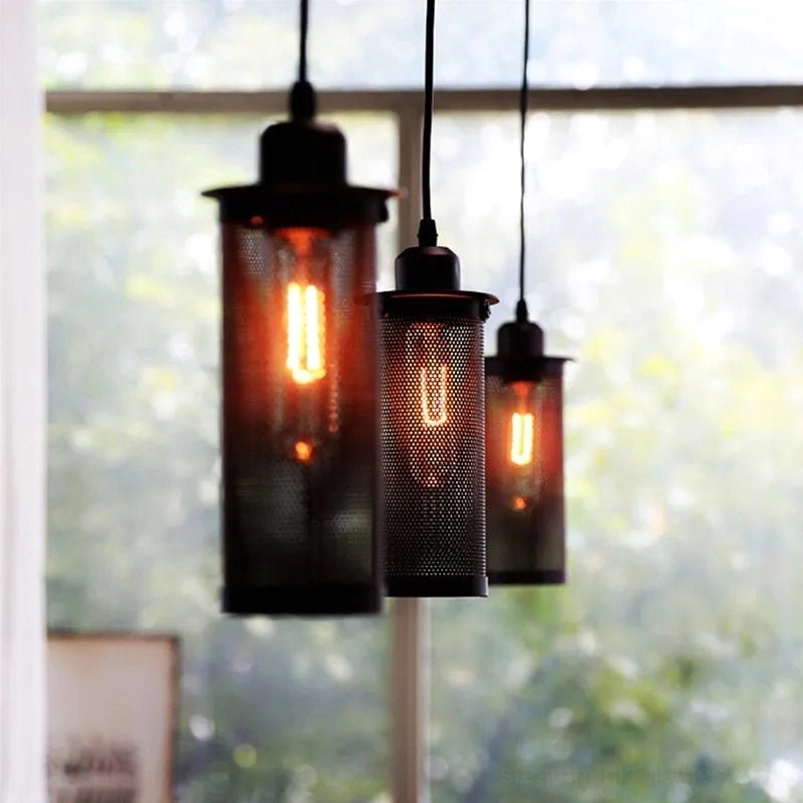 Multiple steampunk pendant lights with dark metal mesh shades suspended at varying heights, warm glowing Edison bulbs creating atmospheric industrial lighting installation