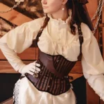 Steampunk pirate corset with brown-black striped fabric and leather trims on Caucasian female model, front left half-body view in vintage indoor pirate setting