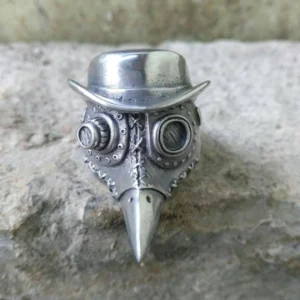 Steampunk plague doctor ring frontal view showing antique silver finish with bowler hat crown, dual mechanical goggles, stitched mask details and pointed beak design on stone background