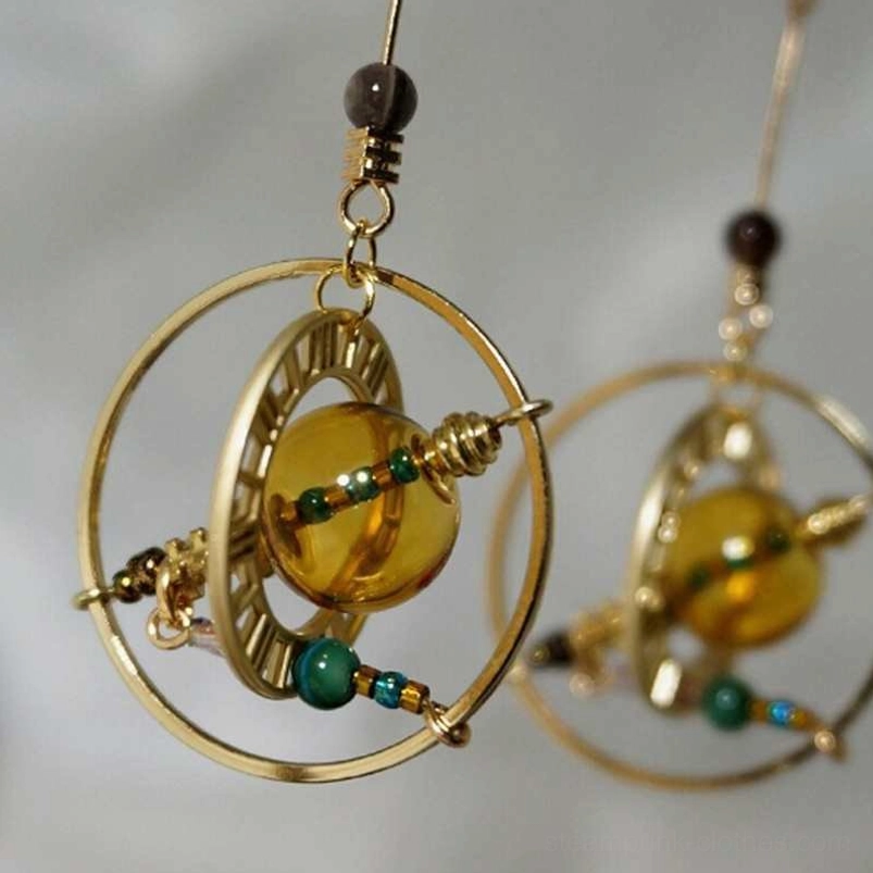 Close-up front view of rotating steampunk planet earrings showcasing polished amber central bead and green-blue micro-beaded decorations