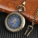 Blue steampunk pocket watch with exposed mechanical gears and carved bronze case, shown at oblique angle with brown leather wallet and metal chain